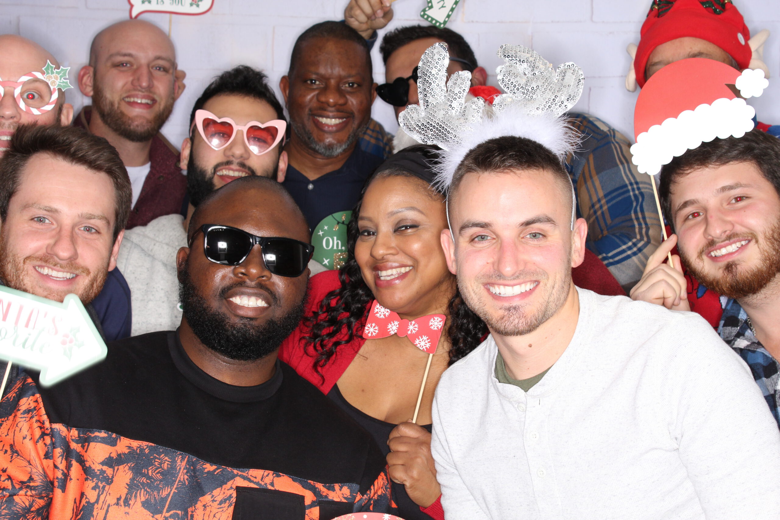 Group of coworkers smiling at a holiday party, wearing festive accessories and posing closely together for a group photo
