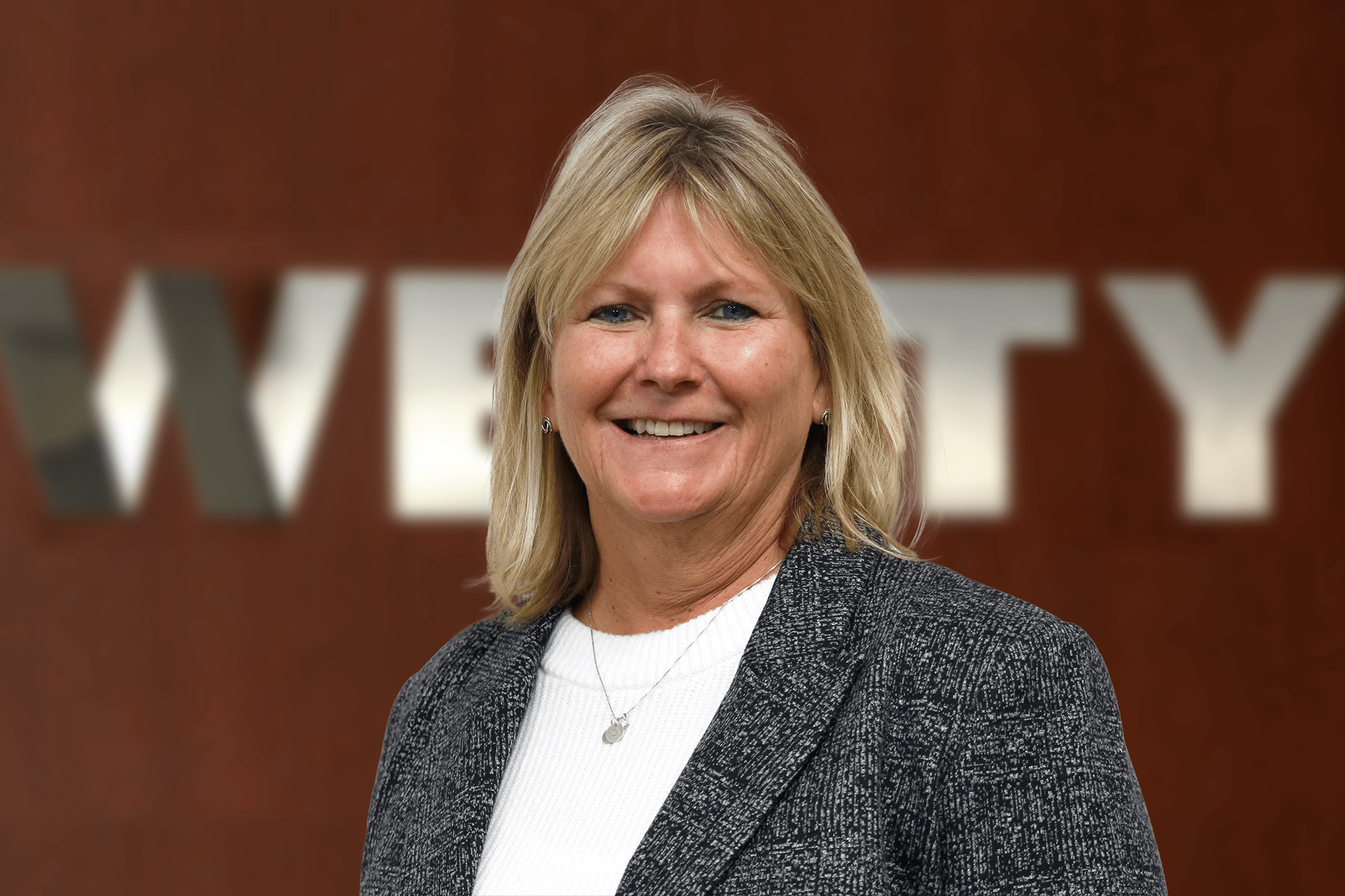 Portrait of a smiling woman standing in front of a blurred WELTY sign.